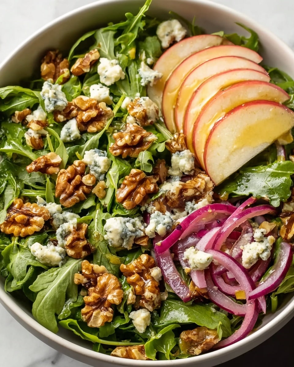 A fresh arugula salad in a white bowl, with a base layer of bright green arugula leaves. On top are thin slices of red apple with white flesh, evenly spread out. Scattered among the apple slices are small chunks of white and blue-veined cheese, and crunchy brown walnut pieces. Thin rings of pale purple-red onions are mixed in, adding color contrast. The whole salad is lightly sprinkled with ground pepper. The bowl is placed on a white marbled surface with a soft grey cloth nearby. Photo taken with an iphone --ar 4:5 --v 7