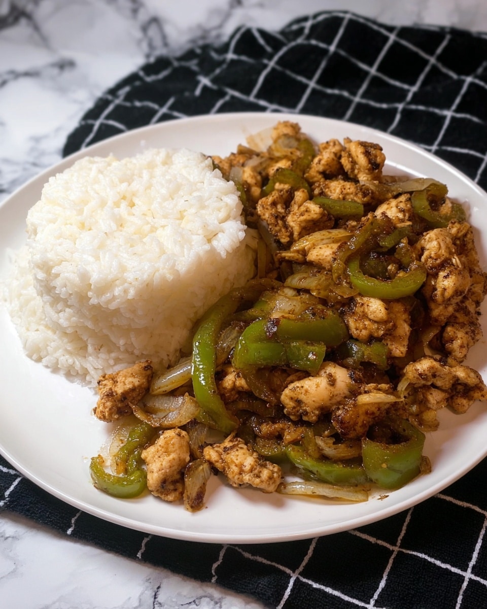 A white plate on a white marbled surface holds a serving of two main layers: on the left and back side, there is a mound of white cooked rice with soft, slightly fluffy texture; on the right and front side, there is a mix of small pieces of browned chicken cooked with sliced green bell peppers and bits of onion, showing a slightly crispy exterior and a tender inside, with a mix of dark and light brown seasoning on the chicken pieces. The background features a black cloth with a white grid pattern. Photo taken with an iphone --ar 4:5 --v 7