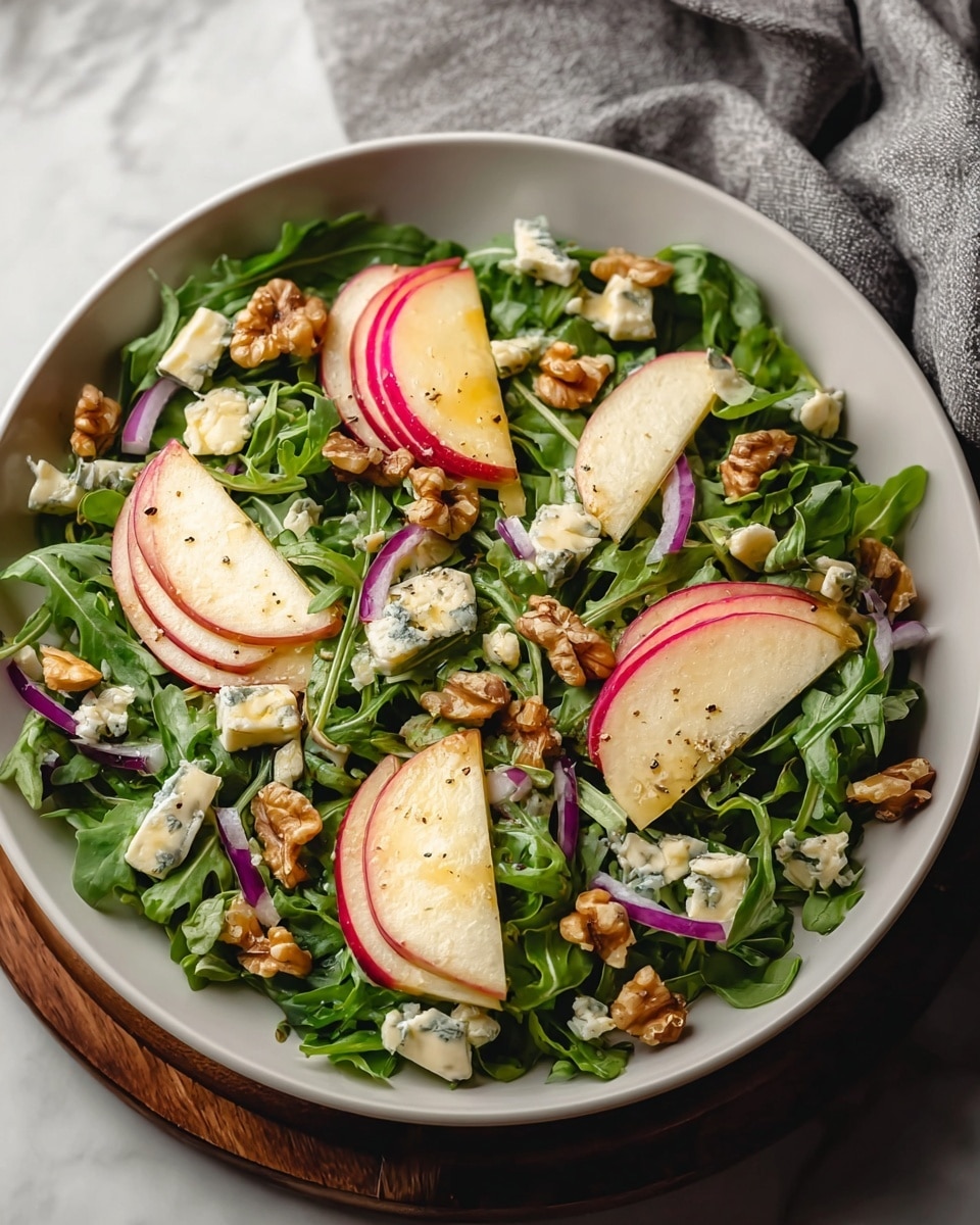 A white bowl filled with a fresh salad showing three layers: the bottom layer is dark green arugula leaves with a soft texture, the middle layer has thin, bright red onion rings and golden brown walnut pieces scattered evenly, and the top layer contains several slices of red apple with white inner flesh, crumbled blue cheese dotted around, and a light drizzle of dressing shining slightly on the ingredients, all set on a white marbled background. photo taken with an iphone --ar 4:5 --v 7