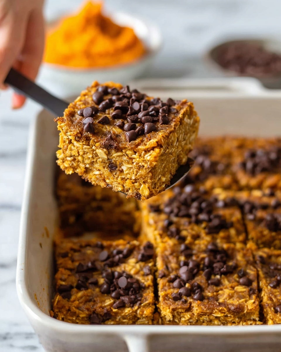 A close-up image shows a thick golden brown baked oatmeal bar being lifted with a spatula by a woman's hand. The bar has a rough texture with visible oats and is dotted with dark chocolate chips on top, giving a contrast of dark brown against the warm golden color. The white dish beneath shows multiple square-cut bars of the same oat mixture, each with scattered chocolate chips. The background features a white marbled surface with a blurred small bowl of orange sweet potato mash. photo taken with an iphone --ar 4:5 --v 7