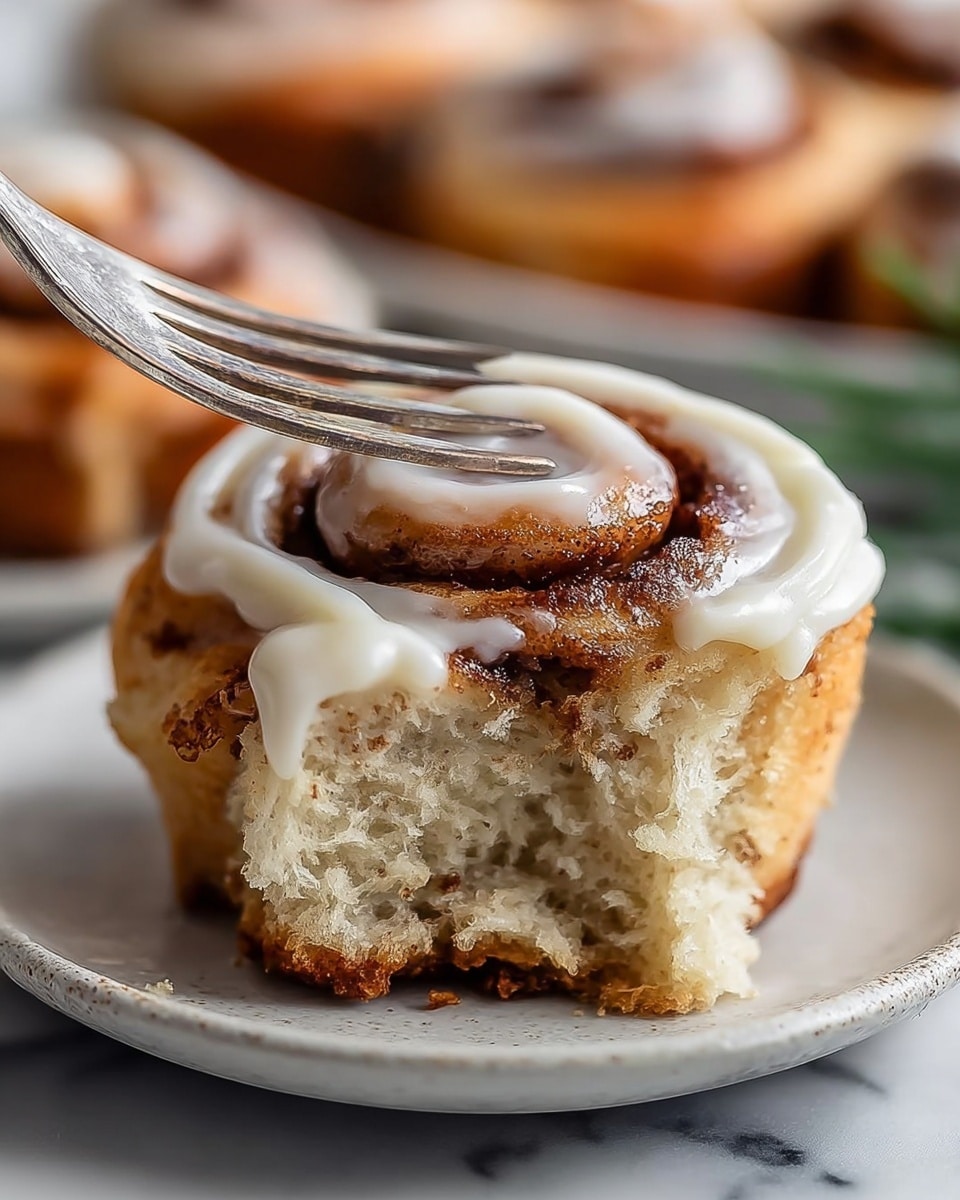 A close-up of a cinnamon roll muffin showing three main layers: the bottom layer is a light brown, slightly crispy muffin base with darker specks, wrapped in a white paper muffin liner; the middle layer is a soft, creamy beige muffin dough with a smooth texture; the top layer is a swirl of golden brown cinnamon filling, topped with a crumbly cinnamon sugar mixture scattered unevenly over the surface. The muffin sits on a white plate with a subtle brown rim, placed on a white marbled texture surface, with out-of-focus muffins in the background. Photo taken with an iphone --ar 4:5 --v 7