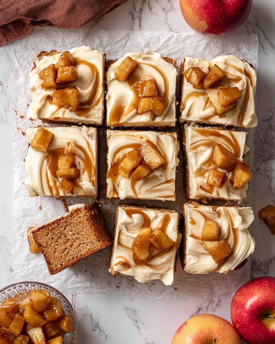 A square cake cut into nine pieces sits on white parchment paper over a white marbled surface. The cake has two visible layers: a moist, dense, light brown bottom cake layer, and a thick top layer of creamy off-white frosting with swirls of caramel or spiced sauce. Small chunks of caramelized apple pieces, golden-brown and glossy, are scattered generously over the frosting, adding texture and color contrast. Two pieces are separated slightly from the rest, revealing the thickness and texture of the cake and frosting layers. Nearby, a small glass bowl holds more caramelized apple chunks, with two red apples and a brown cloth partially visible on the white marbled background. Photo taken with an iphone --ar 4:5 --v 7