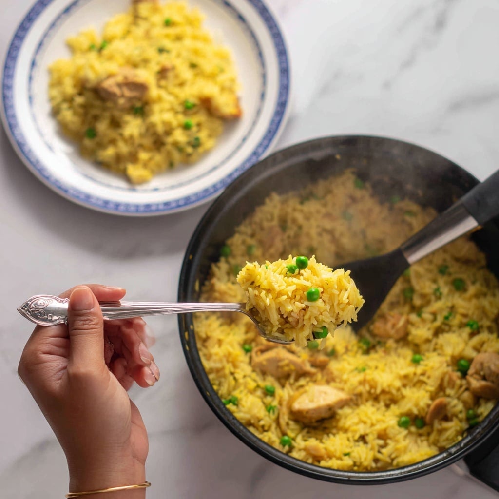 A black pot filled with cooked yellow rice mixed with small green peas and pieces of chicken, with steam rising from the pot showing it's hot. A silver spoon is held by a woman's hand, scooping a portion of the yellow rice with peas out of the pot. In the background, there is a white plate with blue edges containing a serving of the same yellow rice dish. The setup is on a white marbled surface. photo taken with an iphone --ar 4:5 --v 7