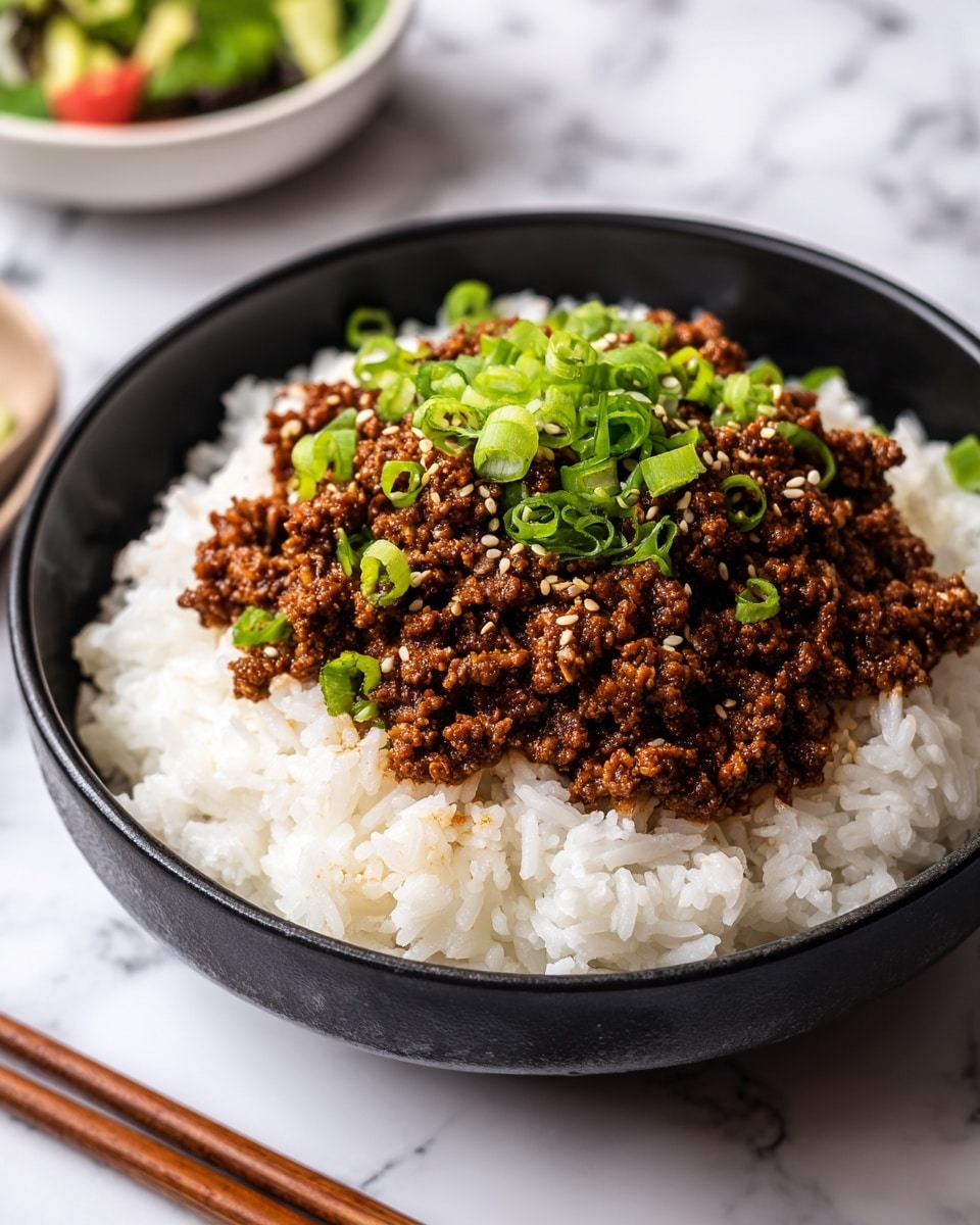 A dark bowl with two visible layers sits on a white marbled texture; the bottom layer is fluffy, white rice covering the whole bowl, and the top layer is a generous amount of brown cooked minced meat mixed with small pieces of green onions, all sprinkled with light tan sesame seeds. In the blurry background, there is a pair of wooden chopsticks laying on the white marbled texture and a black bowl with some colorful food. photo taken with an iphone --ar 4:5 --v 7