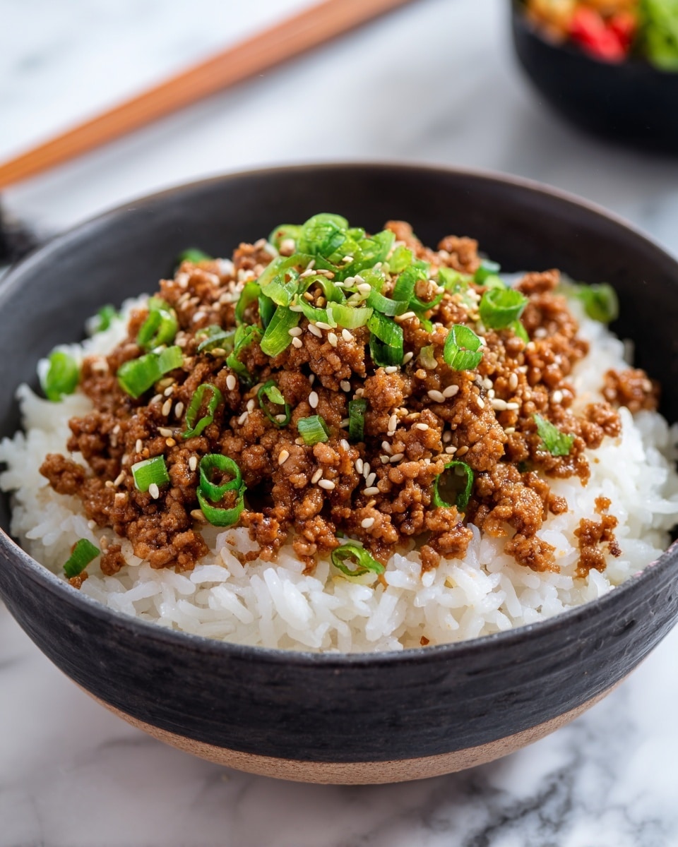A black bowl holds a simple two-layer dish on a white marbled surface, with the bottom layer of soft, fluffy white rice filling most of the bowl, and a generous top layer of finely cooked ground meat in a rich brown sauce. This meat layer is garnished with chopped green onions brightening the middle, and sprinkled with light brown sesame seeds, adding texture and color contrast. In the blurred background, a pair of wooden chopsticks rest on the surface, and a small white bowl with a salad can be seen. photo taken with an iphone --ar 4:5 --v 7