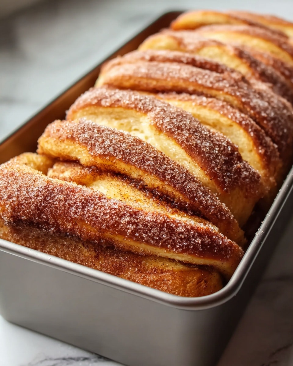 A close-up view of a baked cinnamon pull-apart bread inside a silver loaf pan, showing multiple thick layers of dough with a golden-brown crust on top. The layers are separated by a dark cinnamon filling, and the top is sprinkled evenly with a light dusting of granulated sugar, creating a textured surface. The bread looks soft and fluffy inside with a slightly crispy, caramelized outside. The loaf pan sits on a white marbled texture surface. photo taken with an iphone --ar 4:5 --v 7