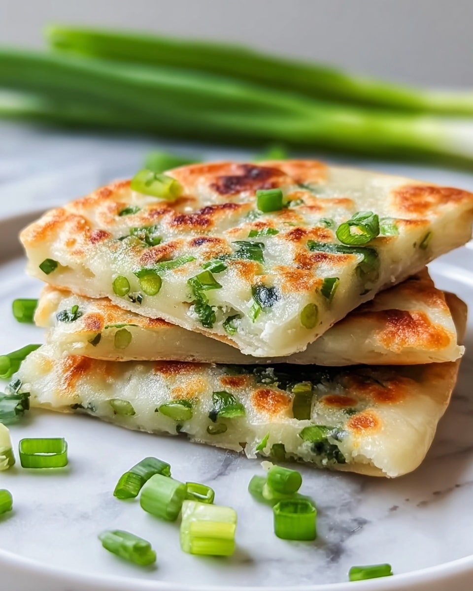 The image shows three square pieces of scallion pancake stacked on a white plate, resting on a white marbled surface. Each pancake is golden brown with crispy, slightly charred spots and dotted with bright green chopped scallions inside and on top. The top pancake is cut in half, revealing a soft, slightly chewy inside filled with bits of green scallions. Some scallions are scattered around the pancakes, and blurred whole scallions are visible in the background. Photo taken with an iphone --ar 4:5 --v 7