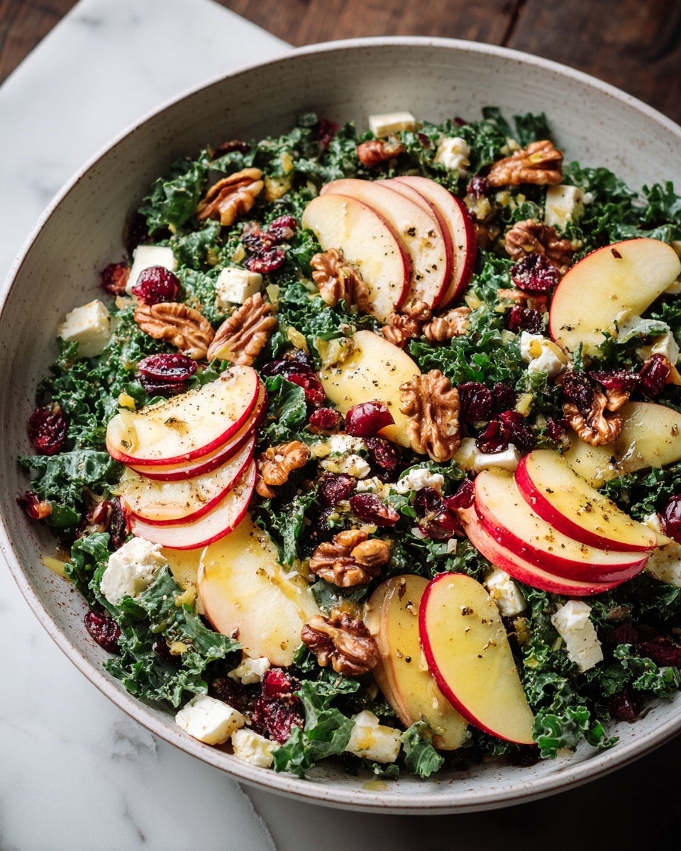 A large bowl filled with a fresh salad showing several layers: the base layer is a bed of dark green kale leaves with a rough texture, topped with thin, crescent-shaped slices of red apple with pale flesh and shiny skin, scattered evenly on top. Mixed among the apple slices are large pieces of glossy, brown pecan nuts with a ridged surface and white crumbly dollops of goat cheese add contrast, sprinkled lightly with specks of black pepper. The bowl is placed on a white marbled surface with loose pecans and a whole red apple nearby. photo taken with an iphone --ar 4:5 --v 7