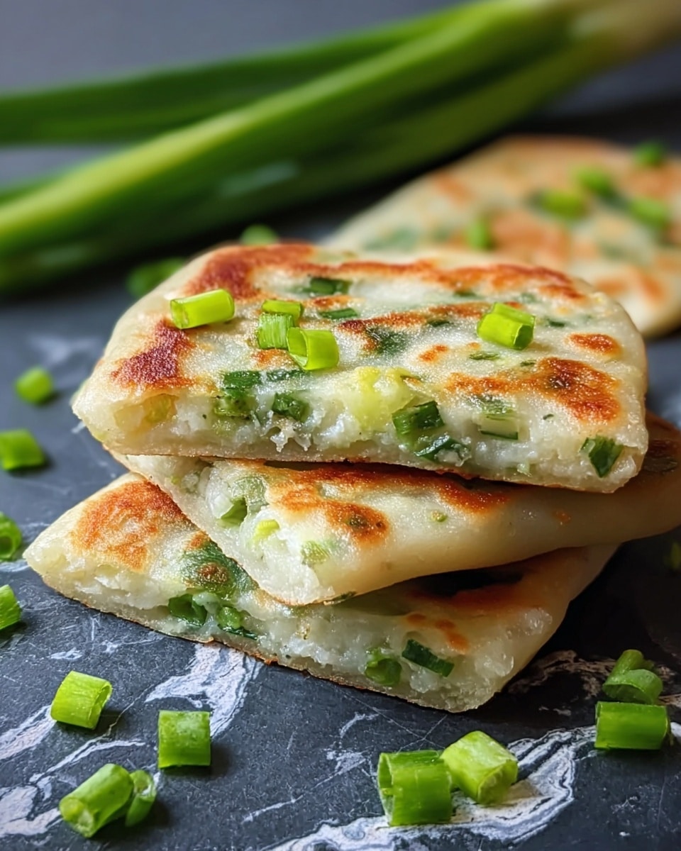 The image shows three square green onion pancakes stacked on a dark surface with a white marbled texture underneath. Each pancake has a golden-brown toasted outside with a soft, slightly translucent dough layer that lets the chopped green onions inside be visible. The top pancake is cut in half, revealing a soft inner layer filled with green onion pieces in a pale dough. Small, bright green onion pieces are scattered on top and around the pancakes. In the background, whole green onions lie horizontally and slightly out of focus. Photo taken with an iphone --ar 4:5 --v 7